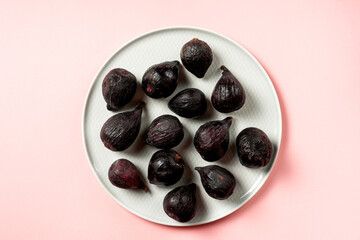 Fresh ripe figs in a plate. Beautiful blue violet fruit on pastel pink background. Healthy Mediterranean fig fruit. Copy space for text. Top view. Vegan concept