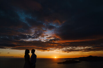 Groom and bride hold hands at sunset against the background of the sea