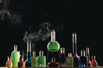  Colorful potions in glass bottles on wooden table. Potion with vapor streaming from bottle. Wizard's Desk. Dark toned foggy background. Halloween concept.