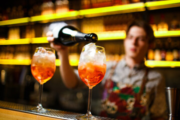 bartender pours orange sparkling wine and aperol cocktail with ice on bright yellow bar counter