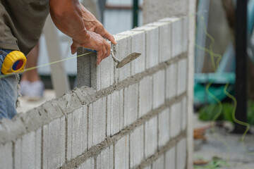 man's hands  of industrial bricklayer with  aluminium brick trowel installing brick blocks on construction site, selective focus at right hand