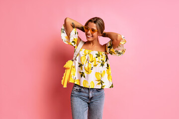 Stylish young blogger woman wearing top with lemon print posing at studio pink background, travel positive mood, Italian fashion style. Summer trendy outfit.