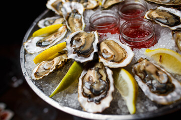 open oysters with lemon and sauce on a tray with ice on a dark background close-up