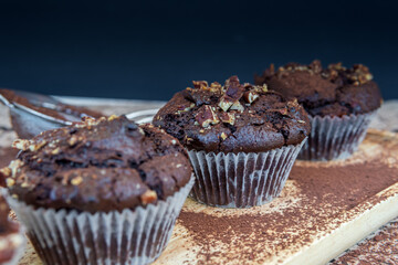 Healthy gluten free chocolate muffins with pecans on a wooden serving board. Homemade, freshly baked delicious cupcakes in baking cups with a crispy top and cocoa powder. Nutrition concept, side view