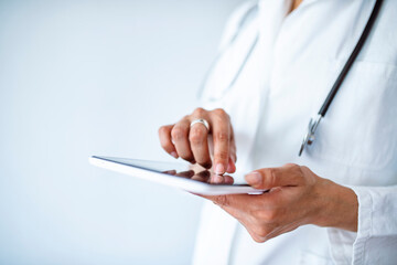 Female doctor using her digital tablet in the office. Close-up of a female doctor using tablet PC. A picture of a doctor holding tablet over white background. Hands holding medical report, copy space.