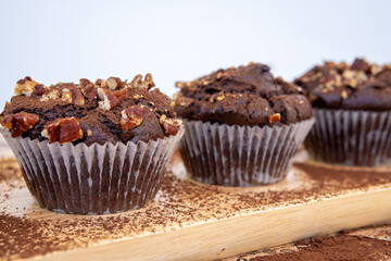 Healthy gluten free chocolate muffins with pecans on a wooden serving board. Homemade, freshly baked delicious cupcakes in baking cups with a crispy top and cocoa powder. Nutrition concept, side view