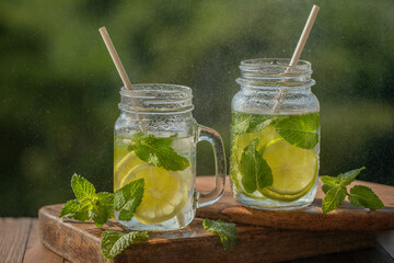 Glasses with lemon water and mint, mojito drink, on a wooden board, outdoors