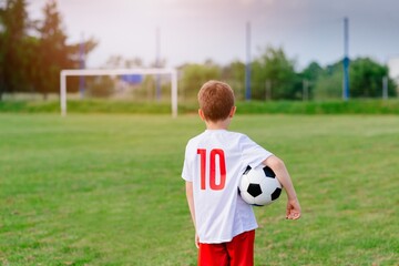 8 years old boy child holding football ball on playing field. Little soccer player.