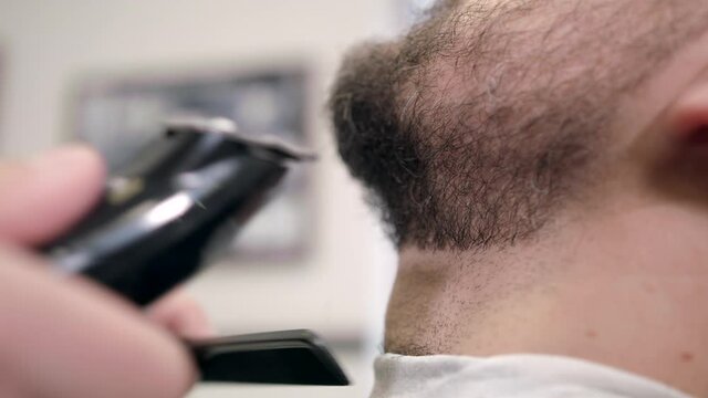 Barber comb and trim beard. Barber shaving beard with electric razor. Professional shaving bearded man in slow motion, extreme close-up shot.