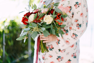 Bride in a bathrobe with a bouquet of flowers stands on the balcony. Close-up