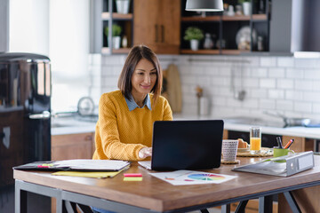 Businesswoman working online from home in front of a laptop computer looking into papers