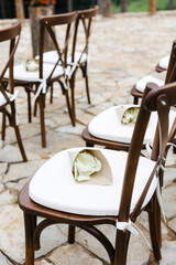 brown wooden chairs with crisscross back. White pillows on chairs and envelopes with white rose petals. against the backdrop of nature on a stone floor. holiday concept.