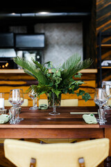 a large wooden table with serving, glasses, green rag napkins and compositions of fresh white flowers. A room with stone walls. Chandelier made of animal horns. holiday concept.