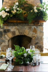 a large wooden table with serving, glasses, green rag napkins and compositions of fresh white flowers. A room with stone walls. Chandelier made of animal horns. holiday concept.