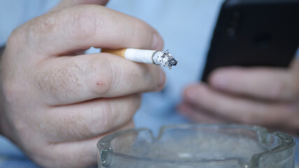 Businessman Smoking a Cigarette, Text Using a Mobile Phone. Relaxed Person Using a Cellphone and Smoking.