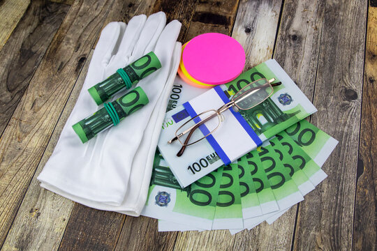 Financial or business concept with a pair of white gloves, eyeglasses and wads and fanned 100 Euro banknotes with colorful circular memo pads over a white marble background in a flat lay view