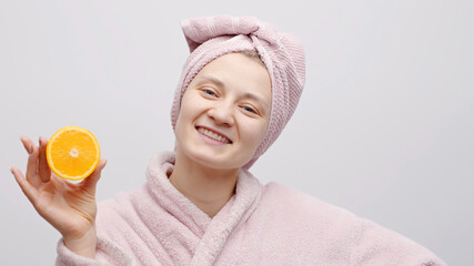 Cheerful girl holding half orange and covering her eye with the orange. The girl is wearing a baby...