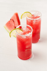 Watermelon cocktails or juice with lime slices and shugar or salt rim in a tall glass on a white deck