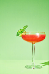 Watermelon cocktail with  cucumber slice and mint leaves in a coupe glass on a green. Minimalistic photo.
