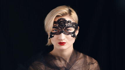Fototapeta premium A blonde model dressed in a masquerade ball costume for the fancy costume party. Wearing A Venetian Masquerade Mask and red lipstick. Closeup headshot. Mysterious girl wearing a Masquerade mask.