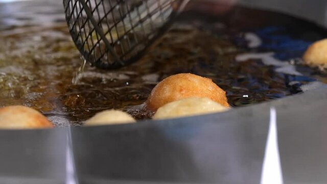 Slow motion of frying lokma dough in heated oil and mixing with sieve, traditional Greek sweet food, 