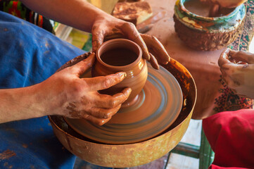 Fototapeta na wymiar Potter makes on pottery wheel clay pot and conducts master class. Hands of master and child close up during work. Ancient national craft
