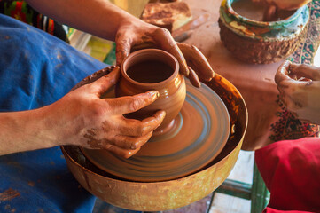 Potter makes on pottery wheel clay pot and conducts master class. Hands of master and child close up during work. Ancient national craft
