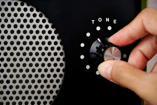 Hand adjusting volume tone control. Use hand to adjust the volume tone at the volume control button of the amplifier.