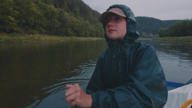 Rafting at rain. Young woman sits on the raft in raincoat and paddles during the rainy day