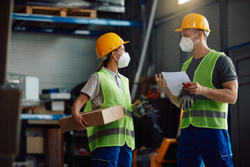 Two workers with face masks talk while working in distribution warehouse.