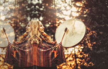 beautiful shamanic girl playing on shaman frame drum in the nature.