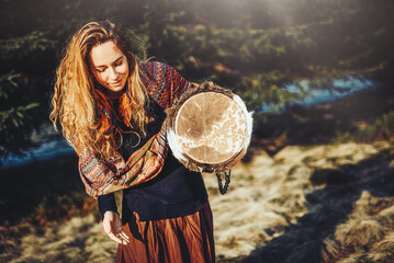 beautiful shamanic girl playing on drum in the nature.