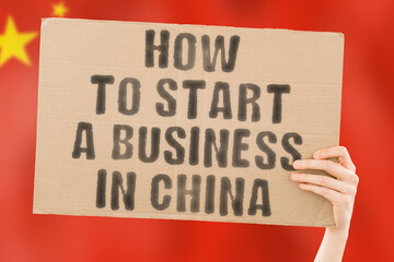 The phrase " How to start a business in China " on a banner in men's hand with blurred Chinese flag on the background. Business. Money. Company. Law. Illegal. Lawyer. Earnings. Job