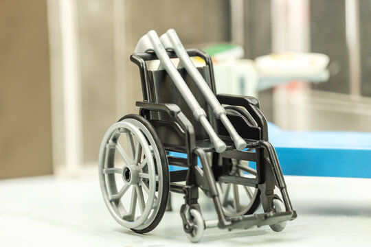 Close-up of a toy wheelchair with toy crutches in front of a sickbay symbolizing the need of auxiliary means / aid / device