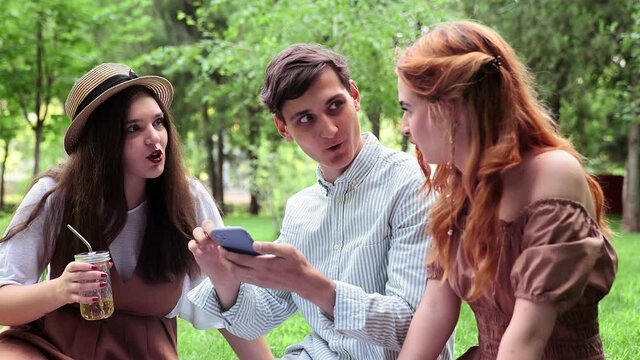 A guy shows two girls photos on his phone in the summer in nature