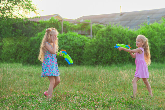 two little girls play in the summer on a green meadow with water pistols