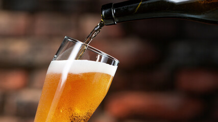 Pouring beer into pint, stylish brick wall on background.