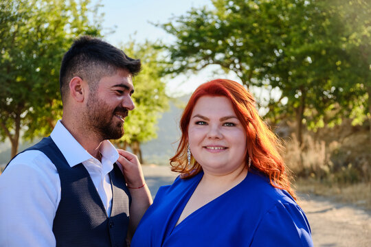 Caucasian plus size red headed woman looks at camera and turkish beloved man look to woman. Mixed race couple on a romantic date. Middle eastern man and caucasian woman marriage or engagement