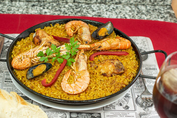 Great mixed Spanish summer paella for two with stewed chicken and prawns, crayfish and mussels, some red pepper and saffron on a table in a tourist restaurant