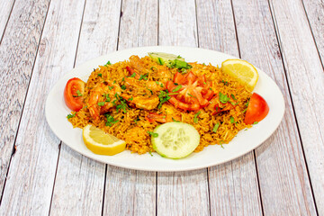 Prawn paella ration for two with raw vegetables for garnish and lots of parsley and lemon to garnish on a white plate