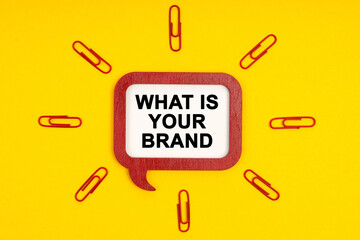 On a yellow background, paper clips and a mental plaque with the inscription - What s is Your Brand