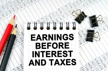 On the table are reports, pencils and a notebook with the inscription - EARNINGS BEFORE INTEREST...