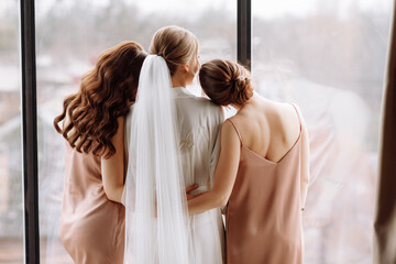 Morning of bride. Gorgeous bride with best bridesmaids are having fun in hotel room near the large window. Sexy bridesmaids in exciting negligee. Wedding morning details. back view