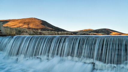 water cascading over a diversion dam at creek in Colorado foothills, sunrise springtime scenery