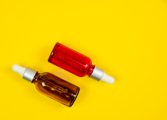 Various amber glass bottles for cosmetics, natural medicine, essential oils or other liquids, on a yellow background, top view.