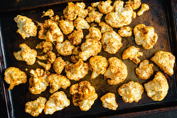 Raw Cauliflower Florets Tossed in a Curry Spice Mixture: Raw cauliflower florets covered in spices on a sheet pan