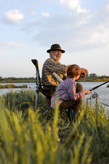 Elderly grandfather and grandson throwing fishing tackle in natural environment, on lake in nature, countryside. Side view on friendly family spending time outdoors, teach to fish. hobby concept