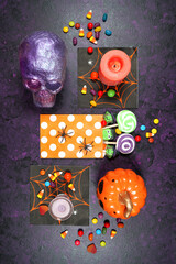 Halloween theme flatlay on textured purple background with purple and orange skull, pumpkin and trick or treat candy. Styled for vertical orientation.