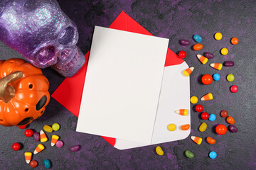 Halloween theme greeting card mockup flatlay on textured purple background with purple and orange skull, pumpkin and trick or treat candy. Product mock up with negative copy space.