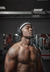 Athletic muscular african american man in wireless headphones listening music with closed eyes during training in gym